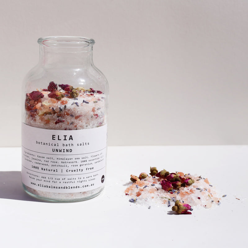 Unwind Botanical Bath Salts 500g in glass bottle, with some of the product next to the bottle.
