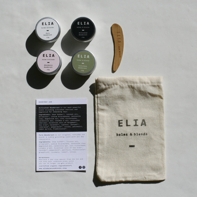 From top left, range of ELIA 15g deodorants, featuring Pure Deodorant (white), Activated Charcoal Deodorant (black), Abundance Bicarb Free (Pink), Conscious Bicarb Free (Green) and ELIA balms & blends bamboo spatula. Ingredients card list and a calico bag