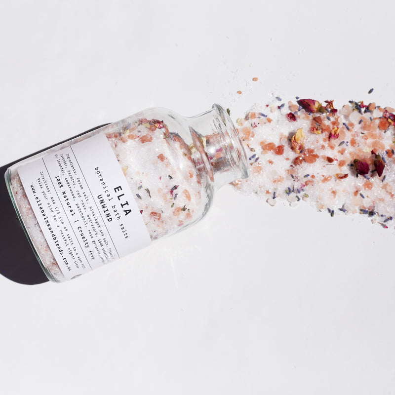 Unwind Botanical Bath Salts 500g in glass bottle, with content spilling out of the bottle.
