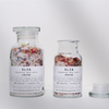 Scale shot of both 500g (left) and 250g (right) Unwind Botanical Bath Salts in glass bottles.
