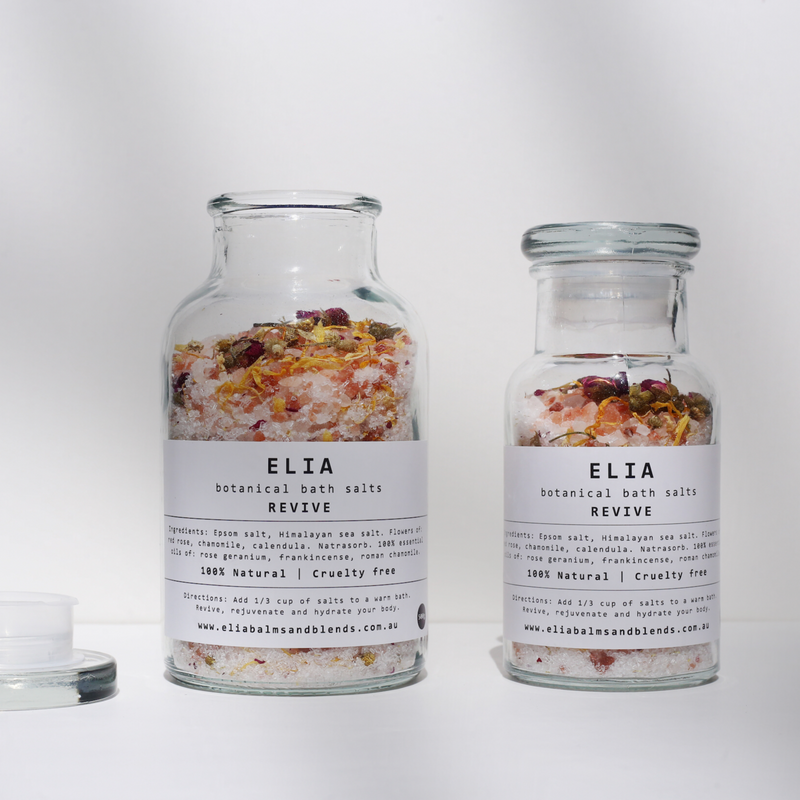 Scale shot of both 500g (left) and 250g (right) Revive Botanical Bath Salts in glass bottles.